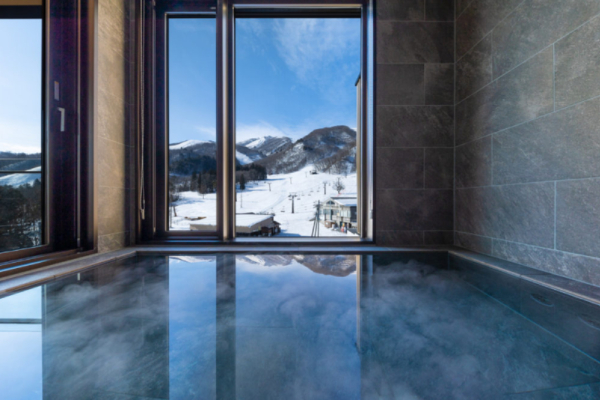 Roka five bedroom penthouse onsen hot spring indoor bath with grey tile walls, ski slope view | Happo Village, Hakuba