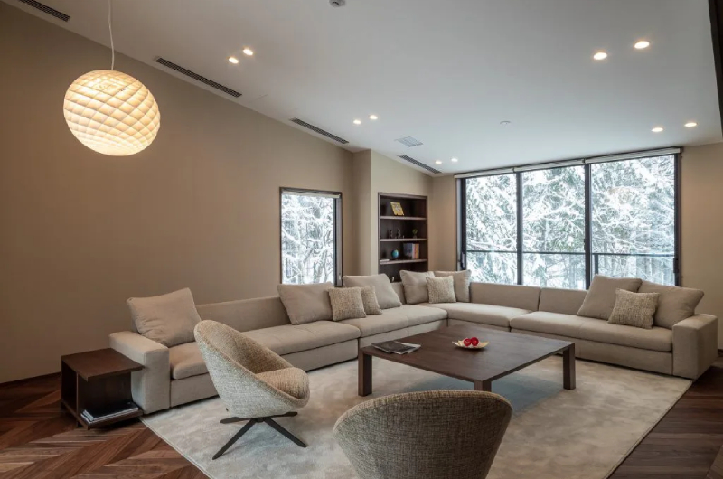 Jade Rabbit living room suite with sofa seating, separate chairs, coffee table, feature lighting, bookshelves and full-height windows | East Hirafu, Niseko